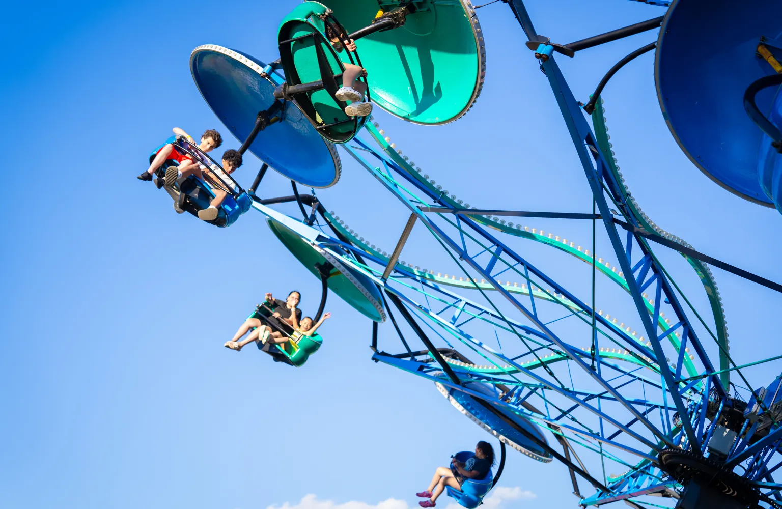 Image of people sitting in seats on flying, spinning ride, with sky in background