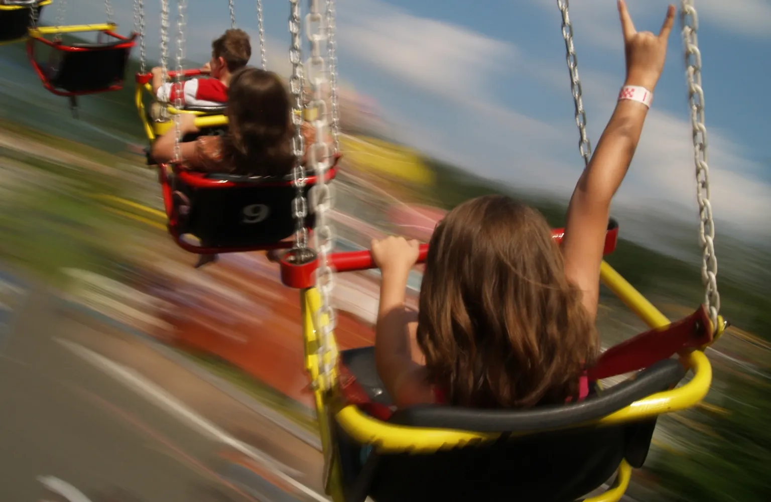 Fast paced shot of children sitting on swing ride, going fast, with arm up in air