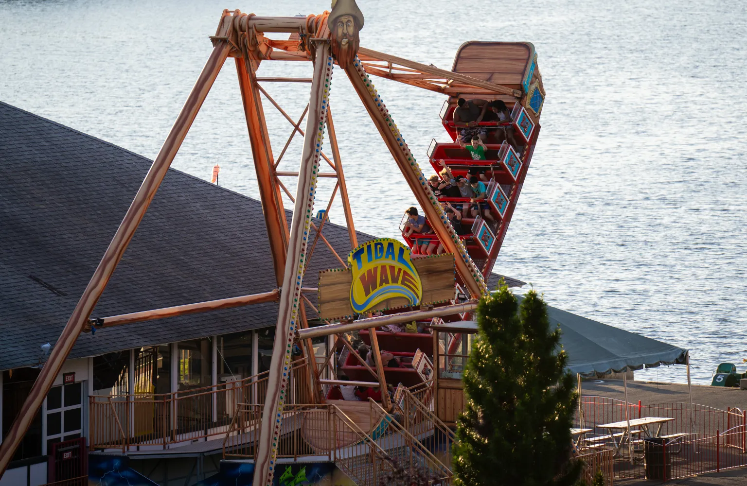 People on Tidal Wave swinging pirate ship ride, with Lake Quassapaug in background