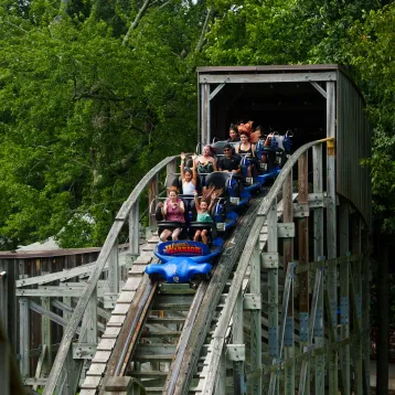 Wooden Warrior roller coaster with people on ride coming out of tunnel and going down drop