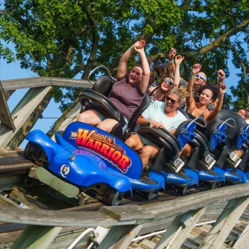 People on Wooden Warrior roller coaster with arms in air and going down drop