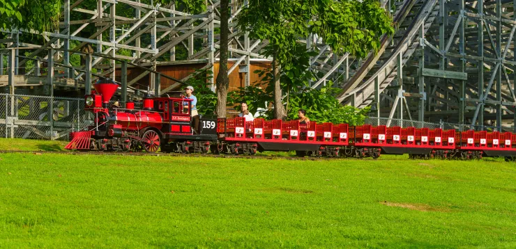 Quassy employee operating Quassy Train in theme park, with people on ride and roller coaster in background