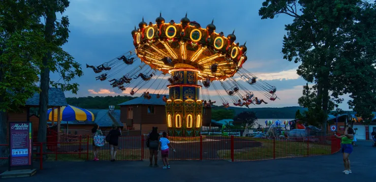 Night view of Aladdin Wave Swinger ride lit up against dark sky, with people in swings on ride