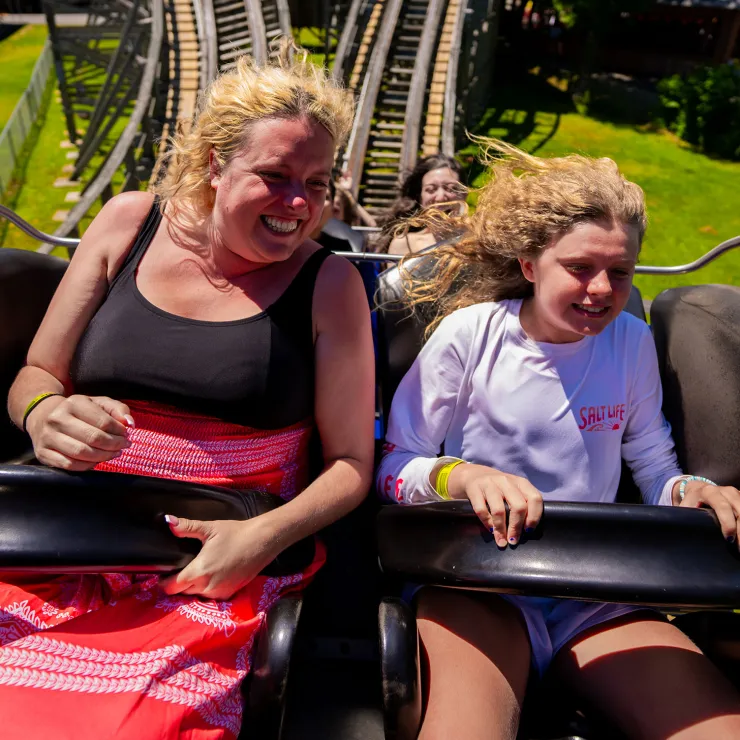 Adult and child on Wooden Warrior roller coaster, holding on to lap bars and smiling