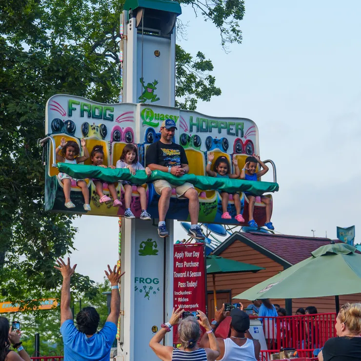 Adult and children on Frog Hopper ride before the drop, with onlookers cheering
