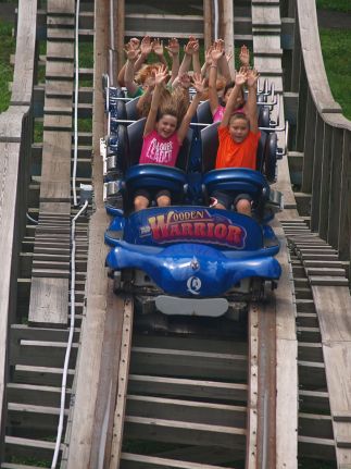 Group of kids smiling with their arms raised ride the Wooden Warrior roller coaster